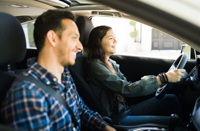Photo of female driving a car smiling with a male passenger also smiling