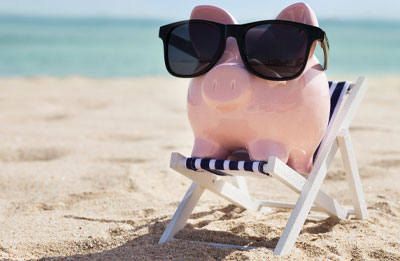 Photo of piggy bank sitting on the beach on a beach chair with sunglasses on