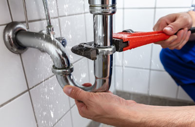 Photo of plumber tightening pipes under leaking sink