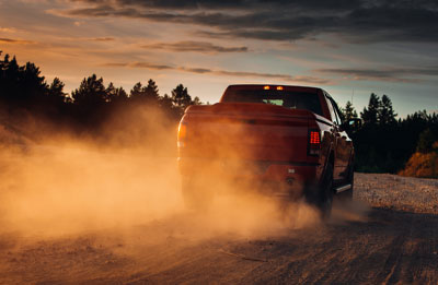Photo of a red truck driving away on a dirt road with dirt blowing up into the air